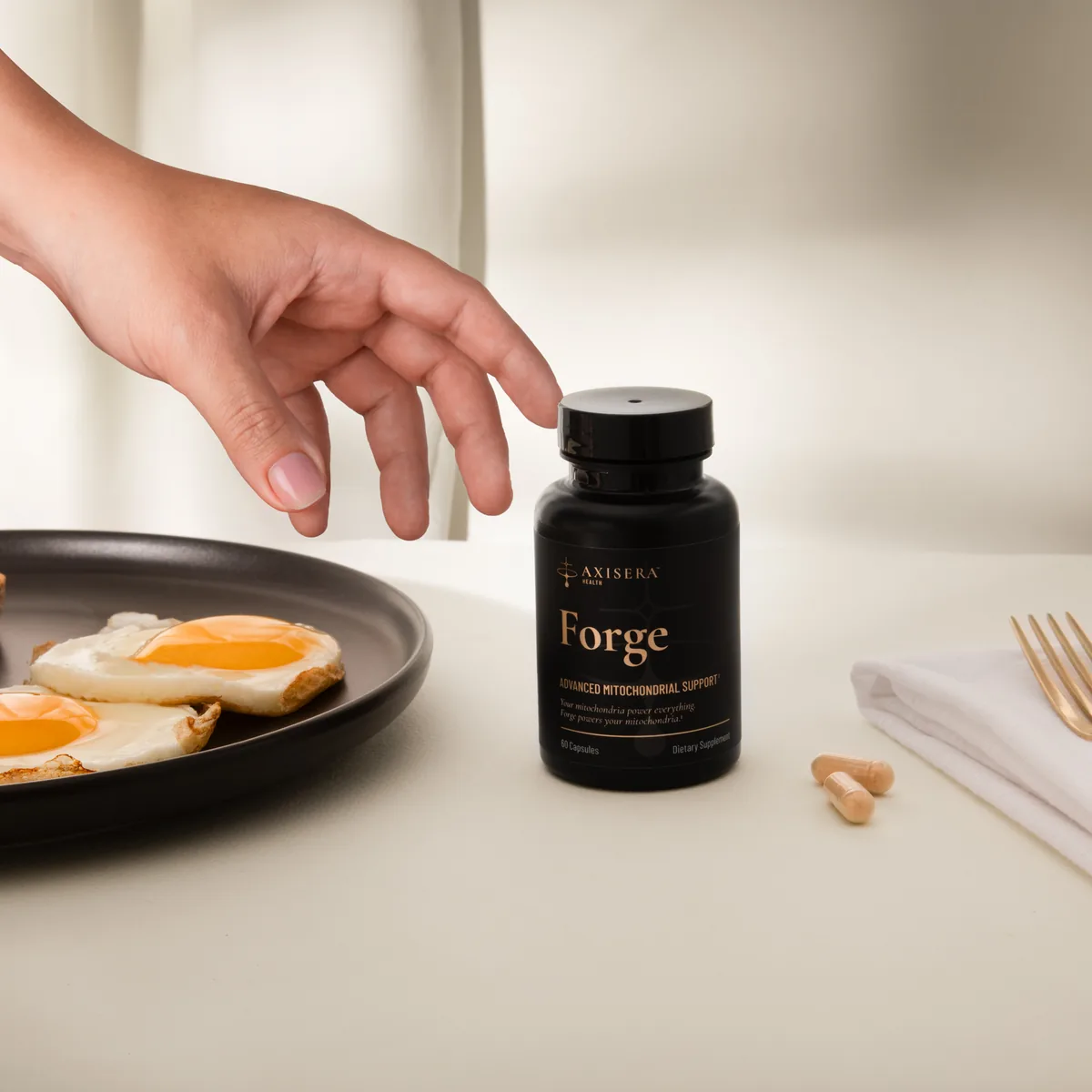 A hand reaching for a bottle of Axisera Forge at breakfast, two capsules beside it